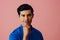 Headshot thoughtful handsome young adult latino man with hand on chin black hair and blue shirt over pink background