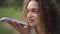 Headshot young brunette curly-haired Caucasian woman smiling talking at smartphone speakerphone. Close-up portrait of