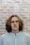 Headshot of young caucasian man looking at camera with blond curly hair. Copy space. Vertical image. Brick wall background