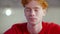 Headshot of young redhead Caucasian man indoors. Close-up portrait of relaxed millennial looking down and talking in