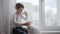 Health care, cute boy drinks clean cool drinking water from glass cup while sitting by window in room