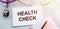 Health check text write on medical notepad with stethoscope, tablets and pen