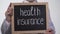 Health insurance text on blackboard in doctor hands, expensive family medicine