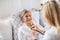 A health visitor examining a sick senior woman lying in bed at home with stethoscope.