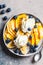 Healthy banana split with mango, chocolate and whipped cream on gray plate, top view