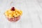 Healthy breakfast in bowl with golden corn flakes, ripe slice cherry on white wood board.