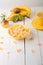 Healthy breakfast with cereal flakes and fruit near vase with flowers on white background. Yellow tone.