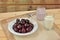 Healthy of breakfast compose of a plate of cherry, a glass of milk and a jar of yogurt on the cloth with wooden background