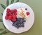 Healthy breakfast.  Fresh blueberries and raspberries with yogurt and cinnamon on a white plate with olive leaves