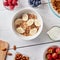 Healthy breakfast ingredients on a white woodwn background. Granola, nuts, berries, milk, banana in bowl , top view