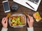 Healthy business lunch at workplace. Salad, salmon, avocado and bread crisps lunch box on working desk with laptop, smartphone,