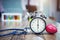 Healthy checking plan concept. Alarm clock with medical instruments stethoscope and red heart on wood table and blurred science l