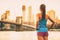 Healthy fit runner woman looking at sunset view of New York City from Brooklyn bridge on summer night. Back of girl in