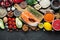 Healthy food clean eating selection: fish, fruit, nuts, vegetable, seeds, superfood, cereals, leaf vegetable on black concrete