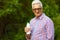 Healthy food concept. Portrait of a mature old man in trendy casual shirt and glasses posing in the park and holding a bottle