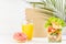 Healthy food set with fresh orange juice, tropical salad in plastic pack, pink donut, packet on in white interior with palm leaf.