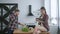 Healthy food, young man prepares useful vegetarian eating on lunch and woman sitting on kitchen table with tablet in