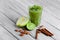 Healthy, fresh green smoothie from exotic fruits on a gray wooden background. Cinnamon sticks, lime, and apple on a desk