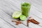 Healthy, fresh green smoothie from exotic fruits on a gray wooden background. Cinnamon sticks, lime, and apple on a desk