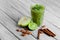 Healthy, fresh green smoothie from exotic fruits on a gray wooden background. Cinnamon sticks, lime, and apple on a desk