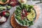 Healthy fresh salad with avocado, greens, arugula, spinach, pomegranate in plate over grey background.