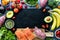 Healthy fruits, vegetables and fish forming a border around a black slate board.