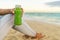 Healthy green juice detox smoothie drink beach woman. Girl holding glass bottle of cold pressed vegetable, juicing trend for