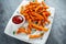 Healthy Homemade Baked Orange Sweet Potato Fries with ketchup, salt, pepper on white wooden board