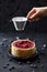 Healthy homemade pastry. Woman hand pouring icing sugar on lingonberry pie with raw berries on black background