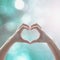 Healthy human hand in heart shape showing love friendship on blurred abstract cool blue green sky color bokeh background