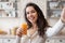 Healthy lifestyle. Cheerful woman making selfie with juice, drinking healthy drink, standing in light kitchen interior
