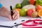 Healthy lifestyle, food and nutrition concept. Close up doctor woman hand holding pen to checklist with fresh vegetables and