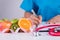 Healthy lifestyle, food and nutrition concept. Close up doctor woman hand holding pen to checklist with fresh vegetables and