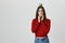 Healthy lifestyle. Isolated portrait of young funny european girl with dark hair in red jumper and denim jeans biting