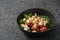 Healthy light salad with cherry tomatoes, mozzarella and frisee in black bowl on concrete surface