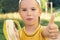 Healthy little boy eating banana. Happy kid enjoy eating fresh fruit and showing thumbs up.