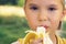 Healthy little boy eating bananaon nature background. Happy kid enjoy eating fresh fruit.