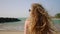 Healthy long hair blowing in wind. Pretty curly model with airy, strong hair posing at coast, sea surf. Young caucasian