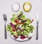 Healthy lunch, fresh salad on a plate with knife fork, oil and salt wooden rustic background top view