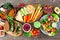 Healthy lunch table scene with nutritious Buddha bowl, vegetables, sandwiches, lettuce wraps and salad, above view over rustic woo