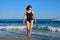 Healthy middle aged woman in sunglasses swimsuit walking along seashore