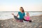 Healthy mother and baby girl doing yoga on beach