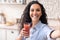 Healthy nutrition concept. Happy latin lady making selfie with tomato juice, drinking healthy drink in kitchen interior
