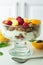 Healthy parfait with greek yoghurt, homemade granola, slices of apricot and raspberries in a glass goblet on a white background.