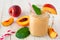 Healthy peach smoothie in a mason jar glass, close up against a white wood background