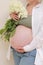 healthy pregnancy. Side view pregnant woman with big belly advanced pregnancy in hands. girl holding big bouquet of
