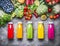 Healthy red, orange, green, yellow and pink Smoothies and juices in Bottles on grey concrete background with fresh organic vegeta