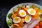 Healthy salad of boiled eggs, ham, tomatoes, carrots, etc. on black granite worktop