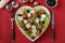 Healthy salad with cherry tomatoes, feta, quail eggs, black olives and microgreens peas on a heart-shaped plate on a red
