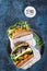 Healthy sandwiches with argula, carrot, cheese, red cabbage, wrapped in craft organic paper on a dark blue background, space for